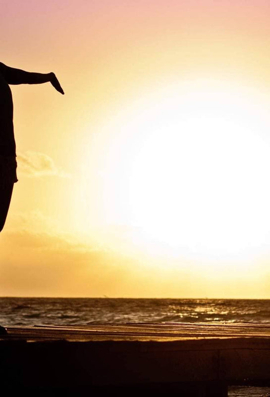 Woman silhouetted at sunset with arms open toward the ocean horizon.
