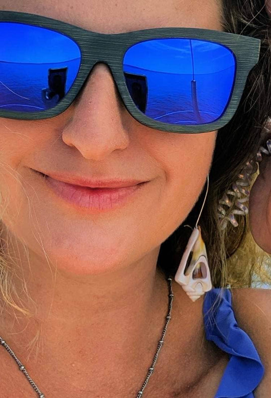 Smiling woman in blue sunglasses and ocean jewelry aboard a sailboat with sea background.