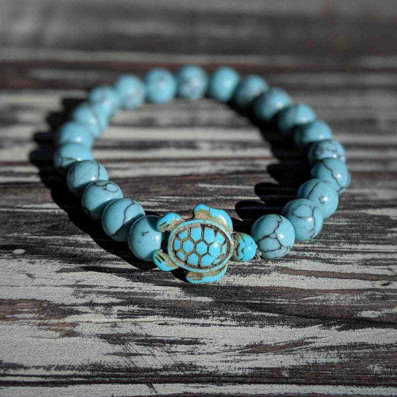 Turquoise beaded bracelet with a turtle charm on a wooden surface