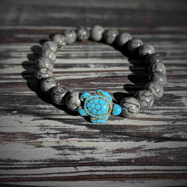 Bracelet with grey leopard agate beads and turtle charm on a wooden surface