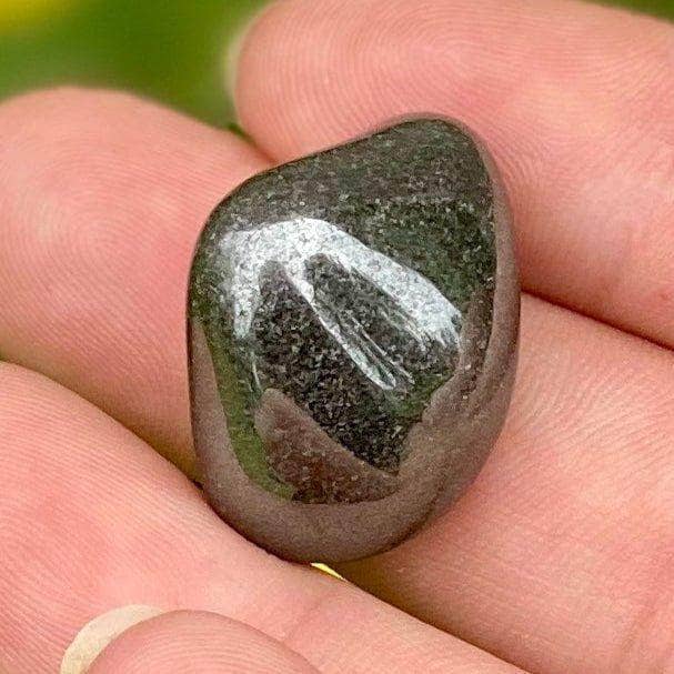 Close up of a polished hematite stones resting on an open palm with bright yellow flowers in the background.
