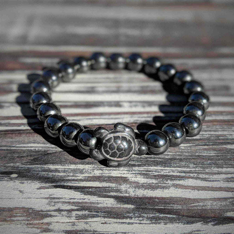 Hematite beaded bracelet with a  turtle charm on a wooden surface