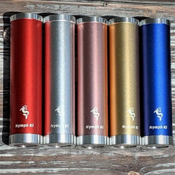 Set of five Nymph Ki kaleidoscopes in red, silver, rose, gold, and blue lined up on rustic wood background.
