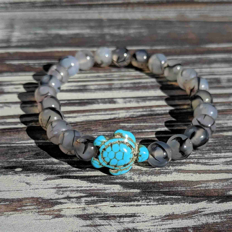 Bracelet with turquoise turtle charm and tourmalinated quartz beads on a wooden surface