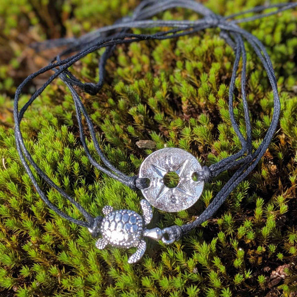 Bracelet with silver turtle charm and circular compass design on a moss background.