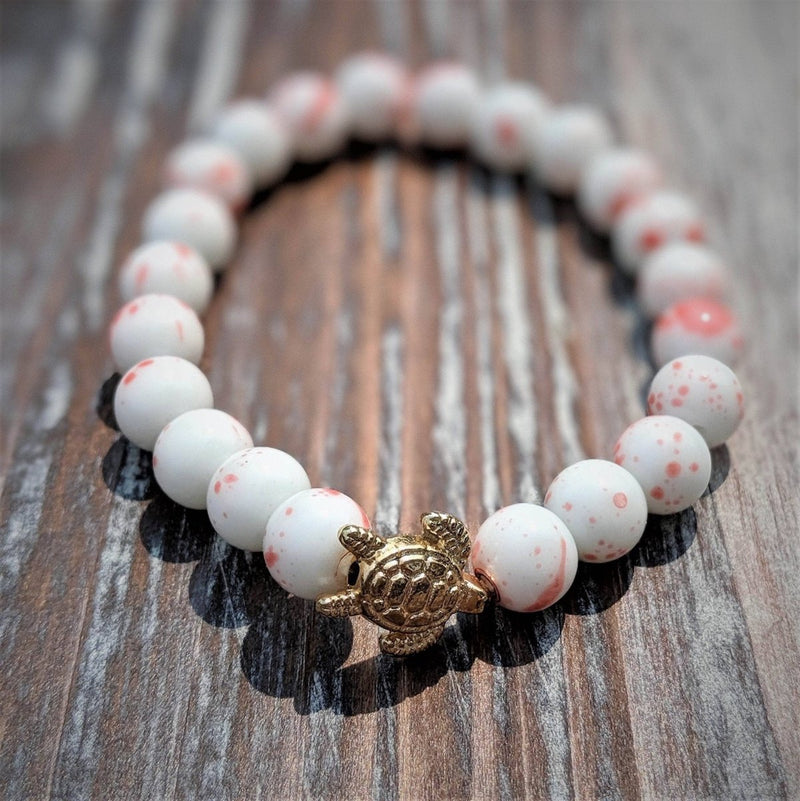 Bracelet with white beads and a gold turtle charm on a wooden surface