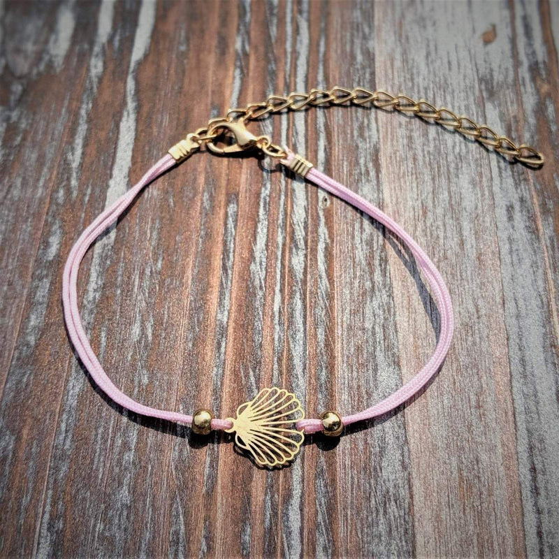 Pink bracelet with gold chain and shell charm on a wooden surface