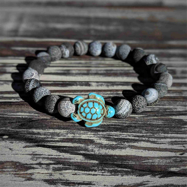 Bracelet with turtle charm and bluish grey weathering agate beads on a wooden surface