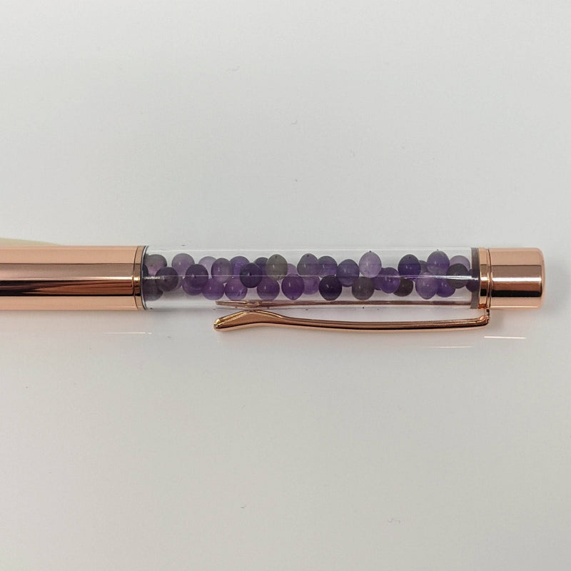 Side view of amethyst-infused rose gold pen showcasing crystal details inside the clear barrel.
