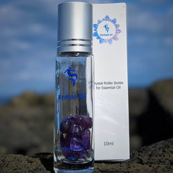 Close-up of amethyst crystal roller bottle outdoors on lava rock with ocean background.  
