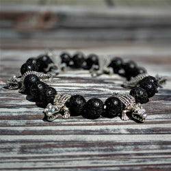 Silver tone gator bracelet with 8mm black lava rock beads on stretch cord, displayed on wooden surface.