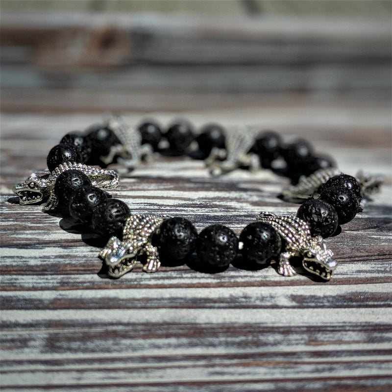 Silver tone gator bracelet with 8mm black lava rock beads on stretch cord, displayed on wooden surface.