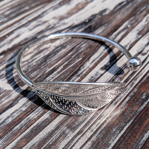 Silver tone adjustable leaf cuff bracelet resting on rustic wood background.