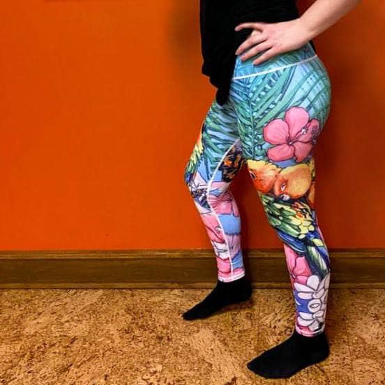 Side close-up of model in Love Bird Leggings showing parrot detail, soft compression fit, and pink hibiscus accent on calf.
