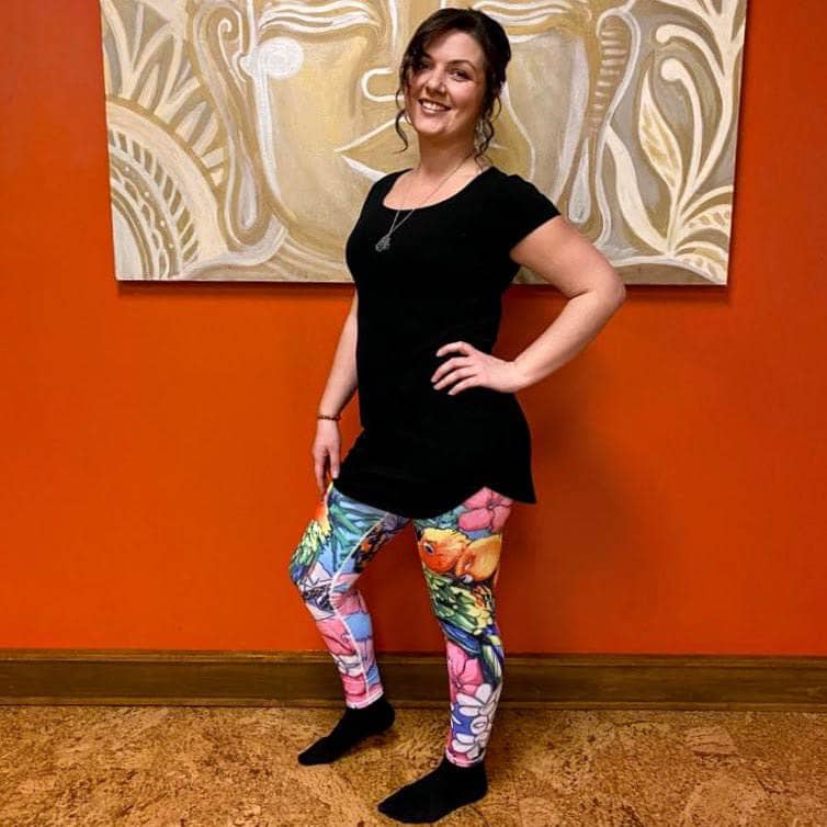 Model smiling in Love Bird Leggings, posing in a confident front-side stance to showcase the vibrant parrot and floral print.
