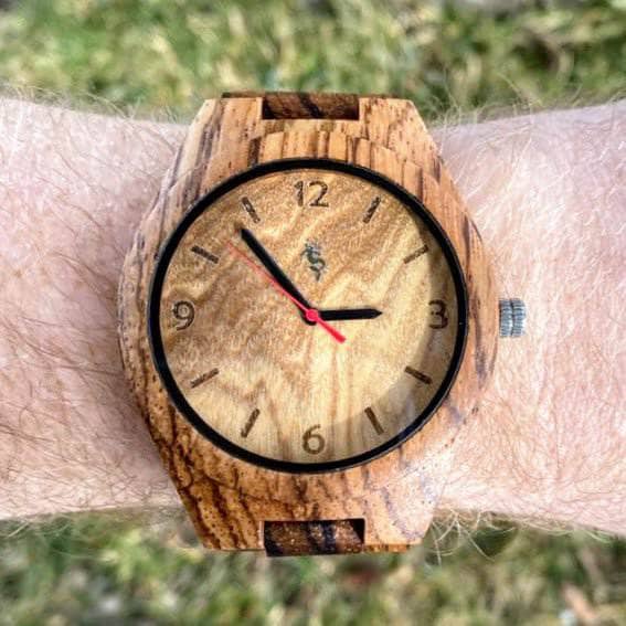 Wood watch on a mans wrist with grass in the background.
