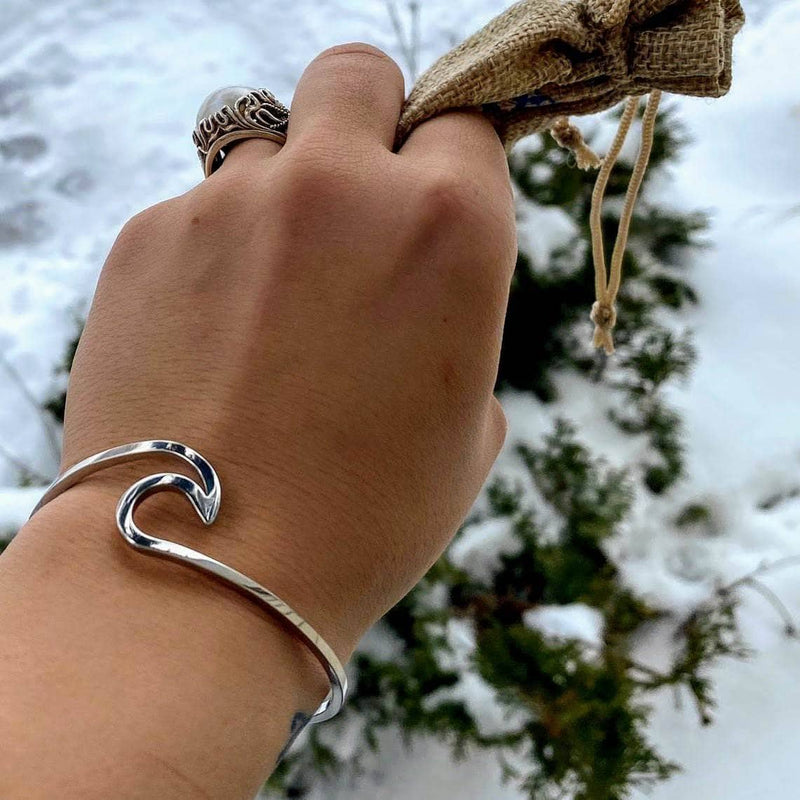 Hand wearing a silver wave-shaped bracelet with a snowy background.