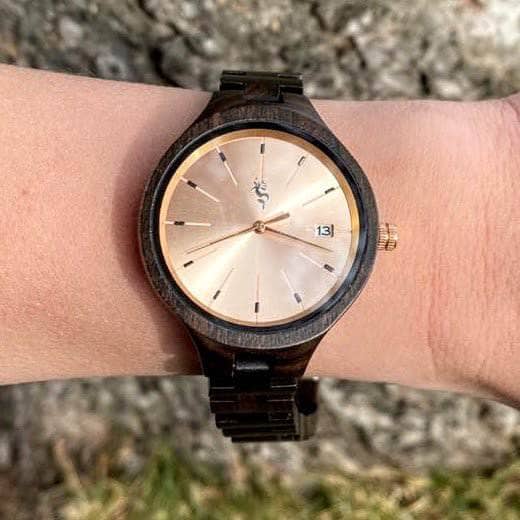Woman's wrist with a wood watch with rose gold face with grass in the background.