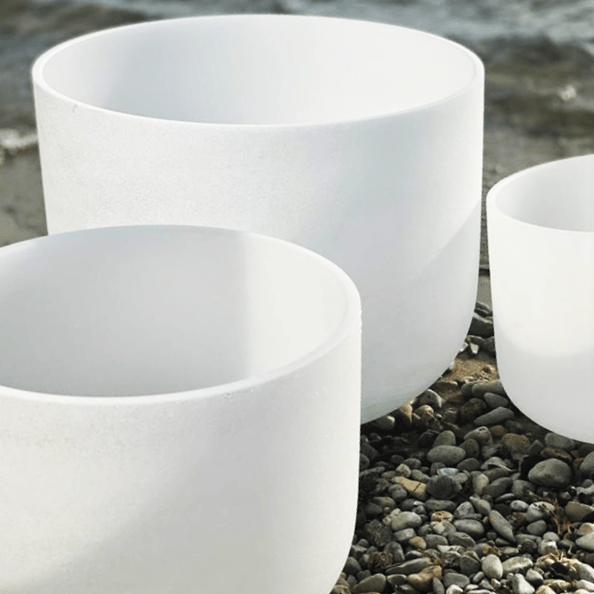 12-inch white quartz singing bowl beside two smaller bowls on a gravel path, used for chakra sound therapy.