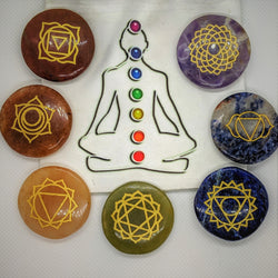 Seven engraved agate chakra stones arranged around a meditating figure illustration.