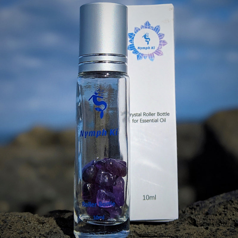 Amethyst crystal roller bottle standing upright on a stone with Nymph Ki label and purple oil chips inside.