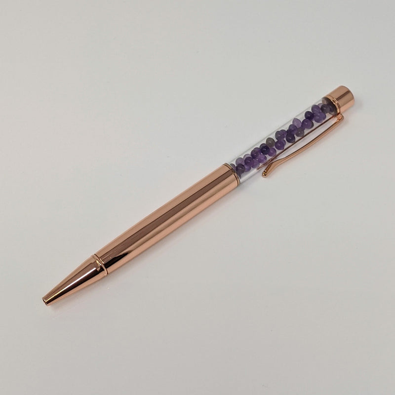 Rose gold pen with visible Amethyst chips laid flat on white background.