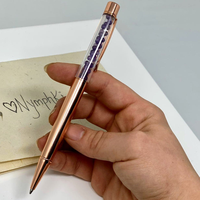 Close-up of Amethyst crystal chamber in rose gold pen held in hand.
