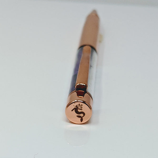 Close-up of Nymph Ki mermaid logo on top of a rose gold pen.