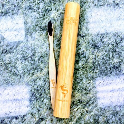 Open bamboo toothbrush case showing the full brush on a natural textured surface.i