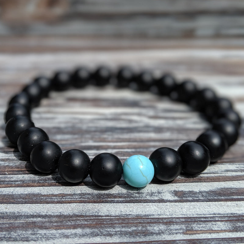  Single black beaded bracelet with 8mm stones on stretch cord, laid flat on wooden surface.