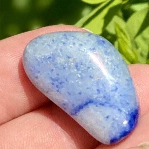 Blue Quartzite crystals in a palm over lush green grass.
