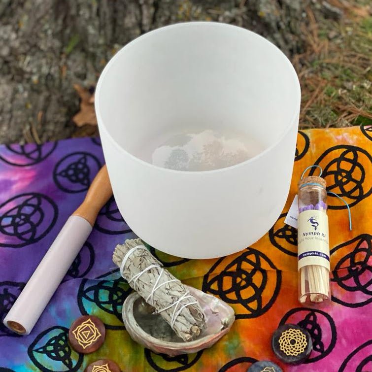 Crystal singing bowl with chakra stones and an abalone shell on a colorful sacred cloth.

