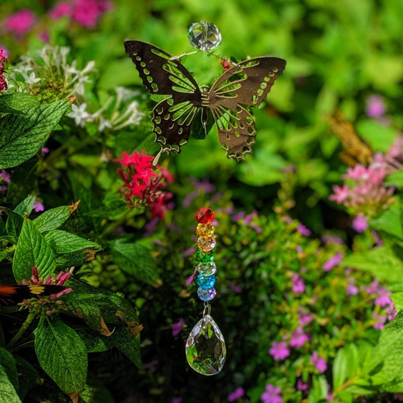  Butterfly-shaped crystal sun catcher with chakra beads and teardrop prism in a colorful flower garden.