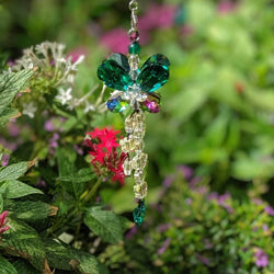 Butterfly sun catcher with chakra-colored crystal beads displayed on stone near water.