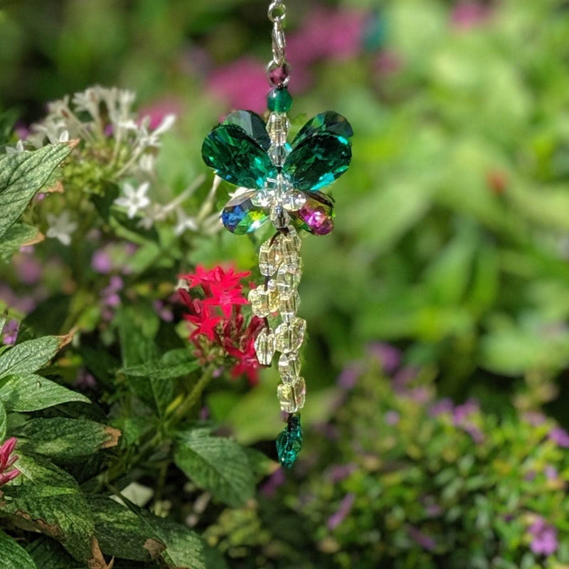 Butterfly sun catcher with chakra-colored crystal beads displayed on stone near water.