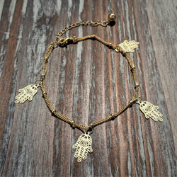 Gold Hamsa Hand charm bracelet on wood background, featuring five protective hand charms.

