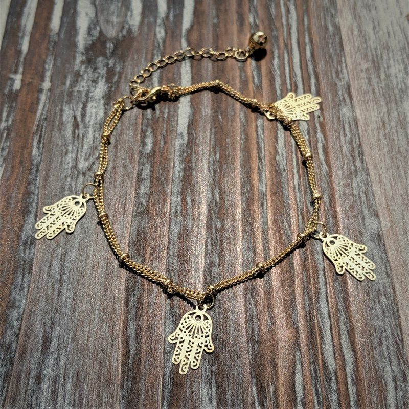 Gold Hamsa Hand charm bracelet on wood background, featuring five protective hand charms.

