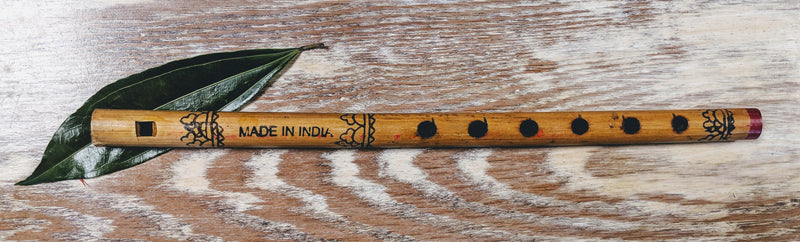  Hand-carved wood flute from India on a rustic surface, showing natural grain and traditional design.