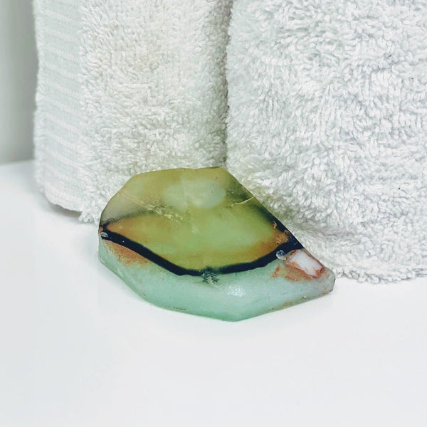 Lemongrass and aquamarine crystal soap resting on a white surface with green hues.