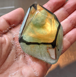 Hand holding a translucent bar of soap with aquamarine crystal and green tint.