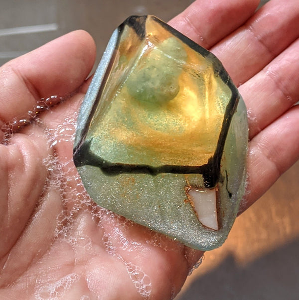 Hand holding a translucent bar of soap with aquamarine crystal and green tint.