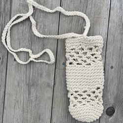 Macrame water bottle holder with long strap, laid flat on a rustic wood surface.