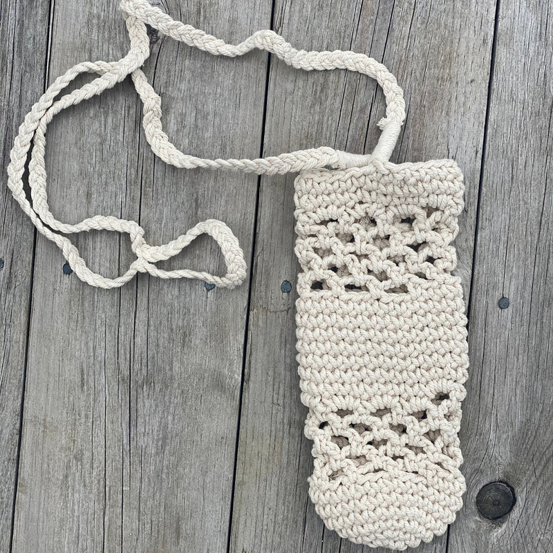Macrame water bottle holder with long strap, laid flat on a rustic wood surface.