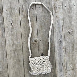 Mini macrame fold-over purse with fringe detail and shoulder strap, shown against a rustic wood backdrop.