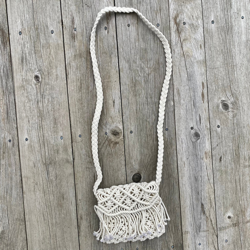 Mini macrame fold-over purse with fringe detail and shoulder strap, shown against a rustic wood backdrop.