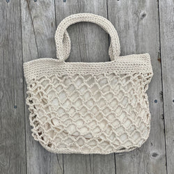 Large macrame purse with woven texture and zipper closure, displayed upright against weathered wood planks.