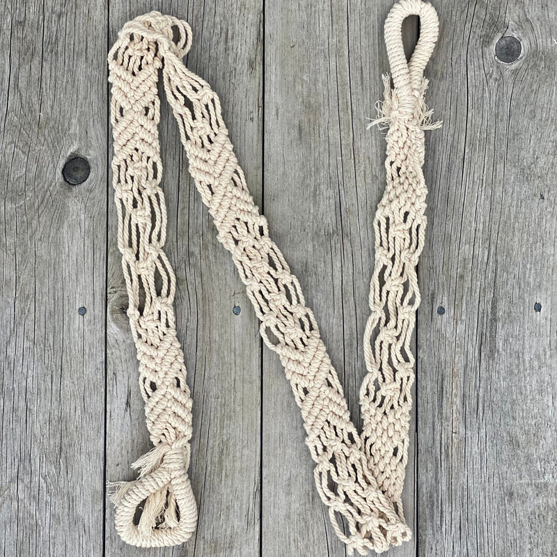 Handwoven macrame yoga strap laid out flat on a wooden surface with looped ends.