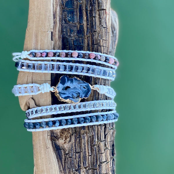 Marble Wrap Bracelet featuring a dark center stone and layers of white, gray, and pink beads wrapped on natural cord over green water – Nymph Ki.