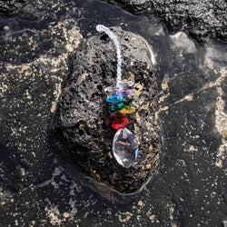 Oval-shaped chakra sun catcher with rainbow prism and chakra crystal beads displayed on natural stone background.