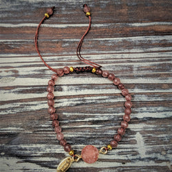 Pink crystal petite bracelet with gold accents on silk cord, styled on rustic wood background.